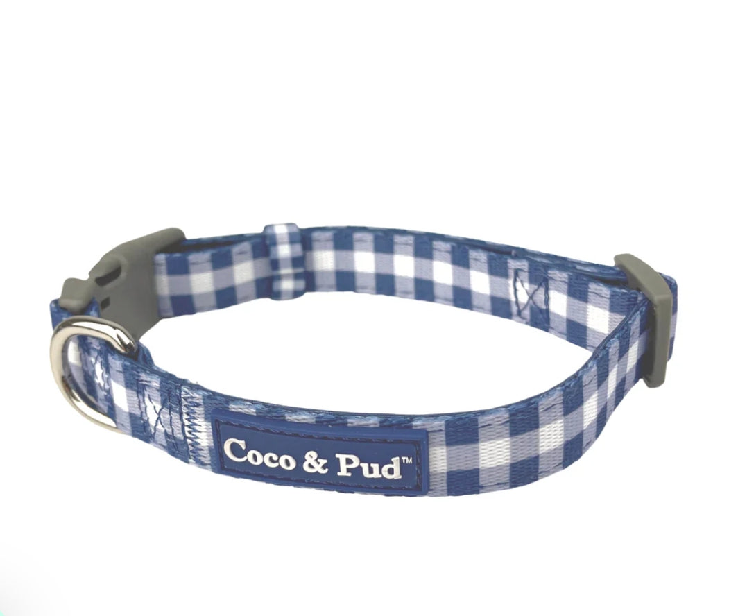 Coco & Pud - A blue and white gingham check dog collar with a gray plastic buckle and a silver metal D-ring, featuring a black fabric label that reads 'Coco & Pud'.