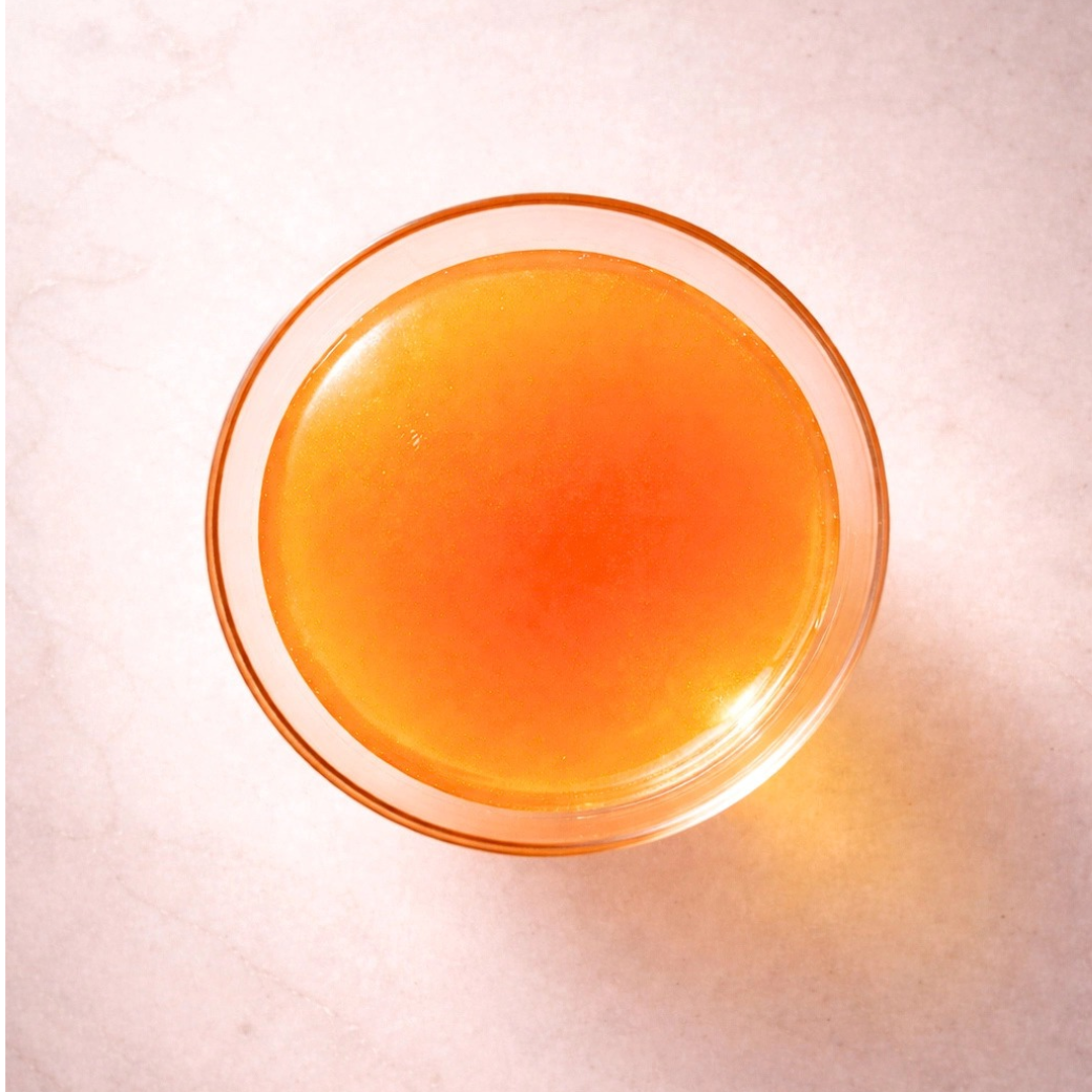 Coco & Pud - A top-down view of a clear glass bowl filled with Brosecco golden chicken broth and sweet carrot tonic/ mocktail - Puptail Society 