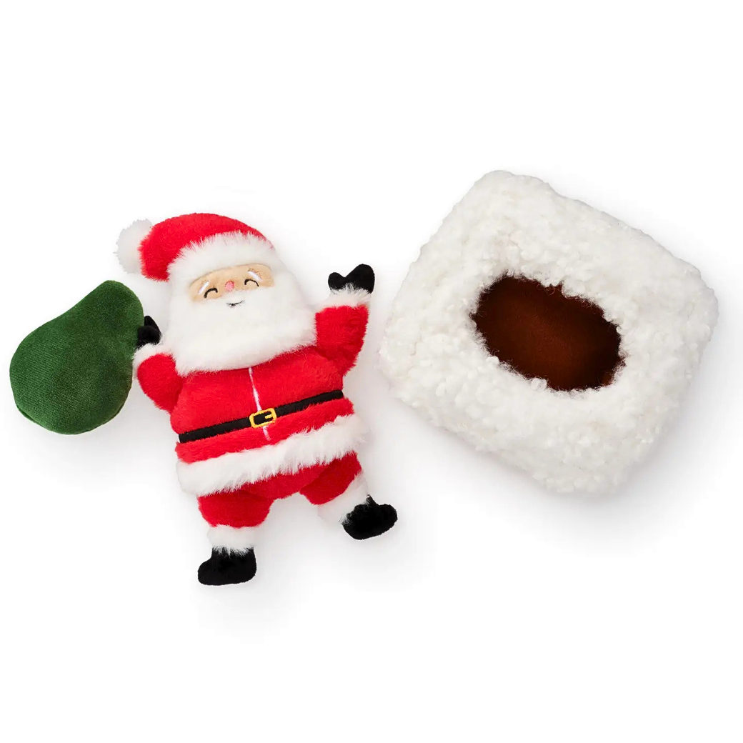 Coco & Pud - Here Comes Santa interactive dog toy. A plush Santa Claus in a red suit, white fur trim, black gloves, a green sack,with a white fluffy snow laden brick chimney flat lay - The Foggy Dog
