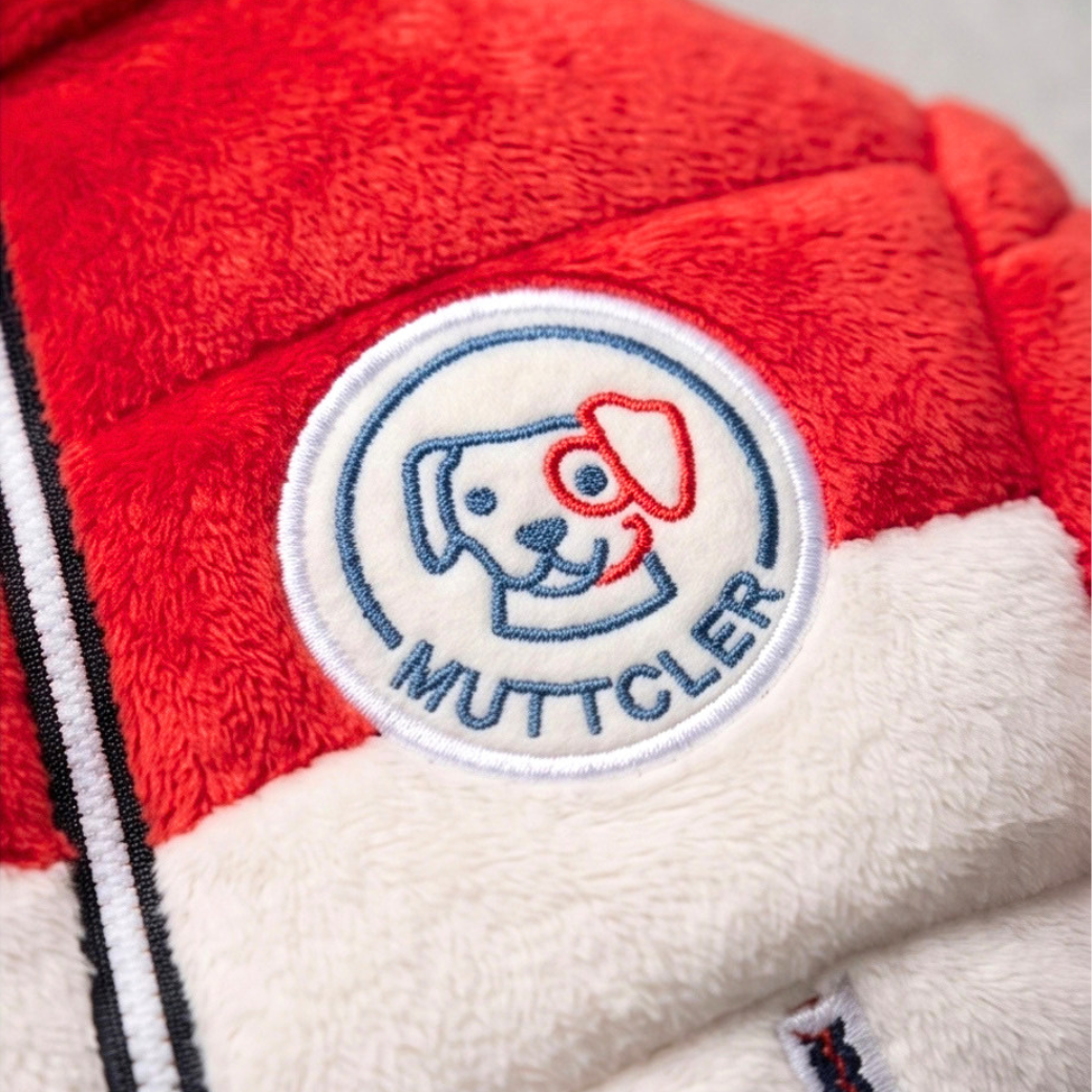 Coco & Pud - A close-up detail of a red and white plush jacket featuring a circular embroidered MUTTCLER logo patch with a dog illustration - Haute Diggity Dog