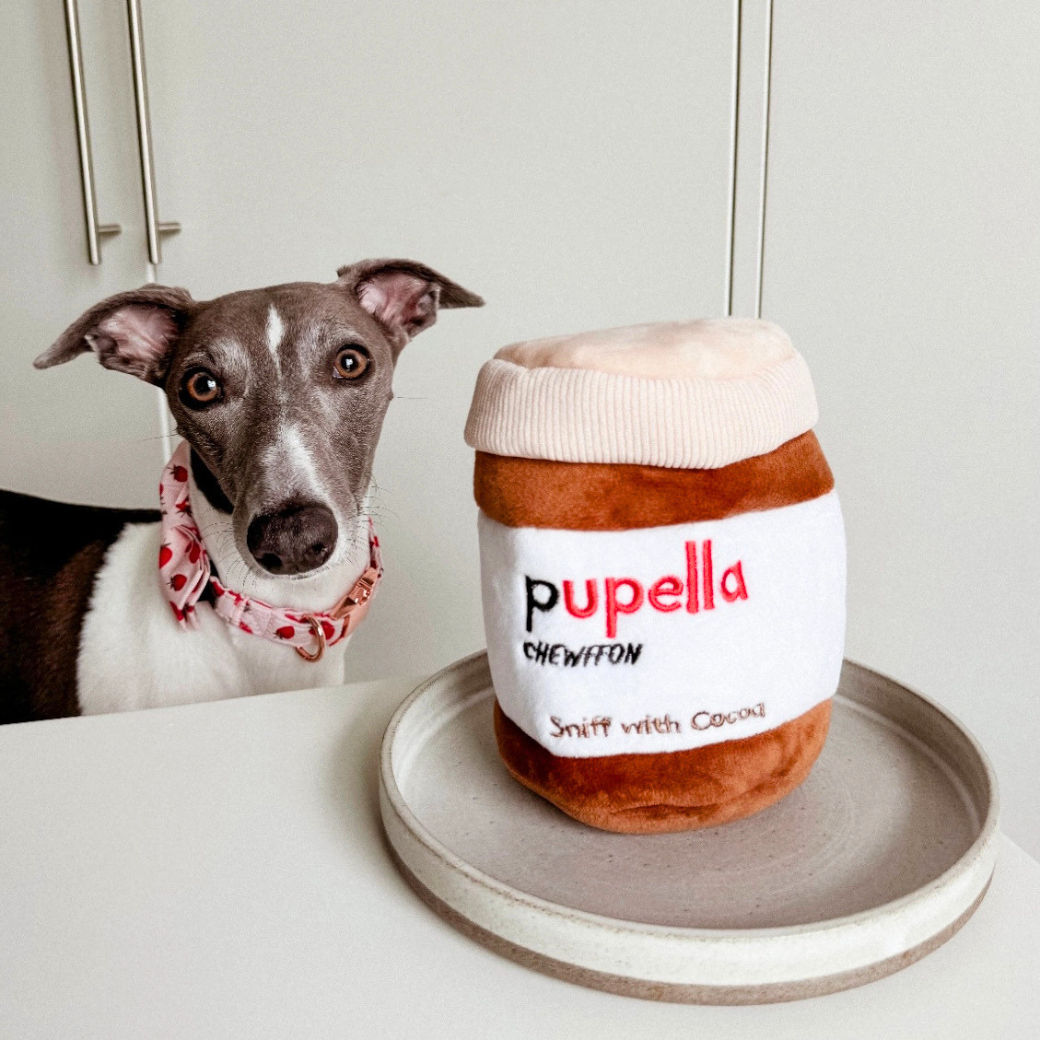 Coco & Pud - Pupella interactive dog toy shaped like a jar of Nutella next to a grey and white Italian Greyhound dog. The toy features a plush brown body, a cream-colored lid, and a white label with the text 'pupella' - Chewffon