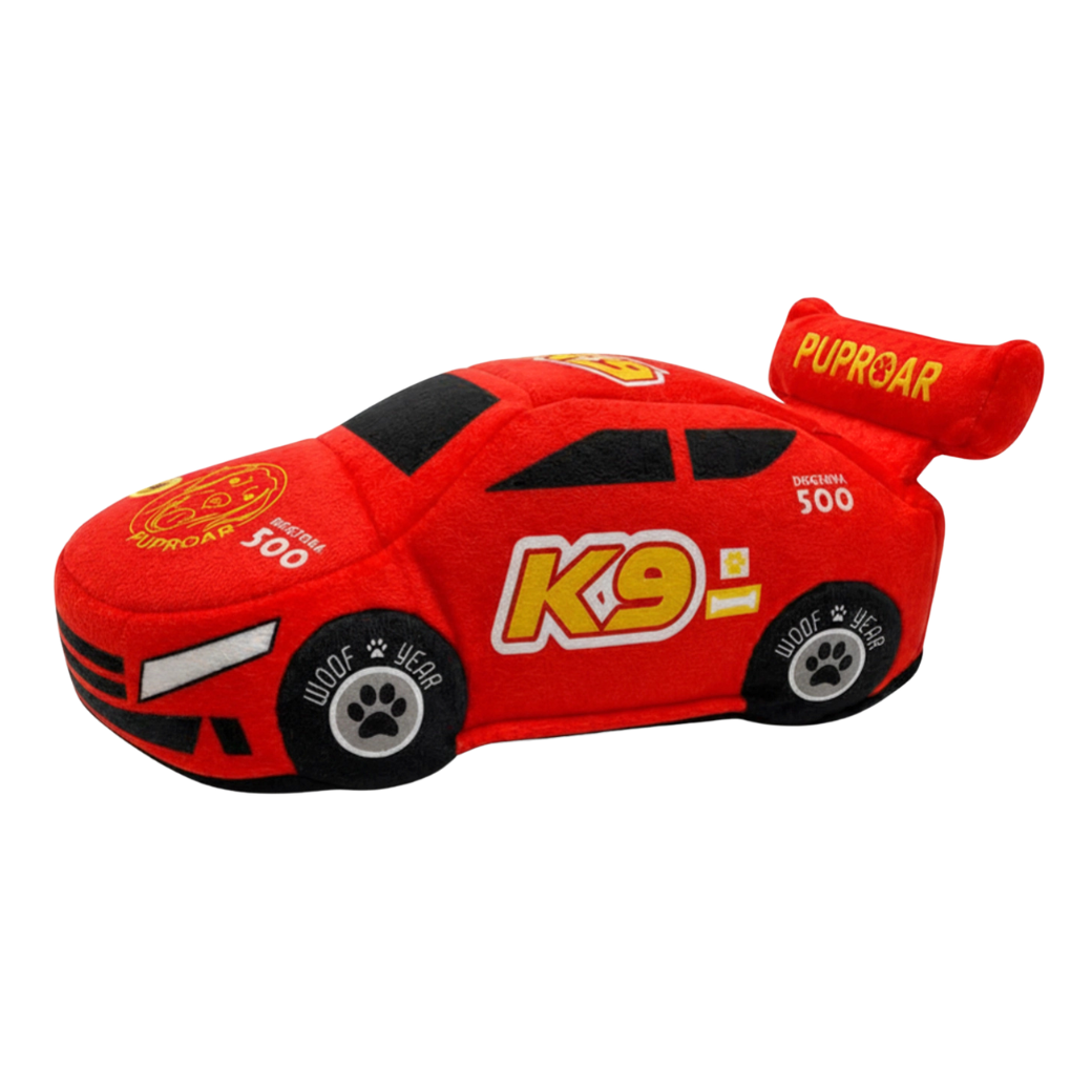 Coco & Pud - Stock car Racing Car plush dog toy. A red plush toy race car with black wheels and yellow and white racing graphics, including 'K9' on the side and 'PUPROAR' on the rear spoiler. Puproar